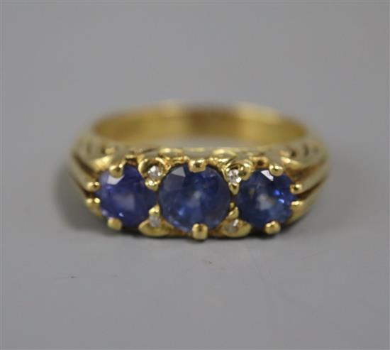 A modern Edwardian style 18ct gold and three stone sapphire ring with diamond chip spacers, size O.